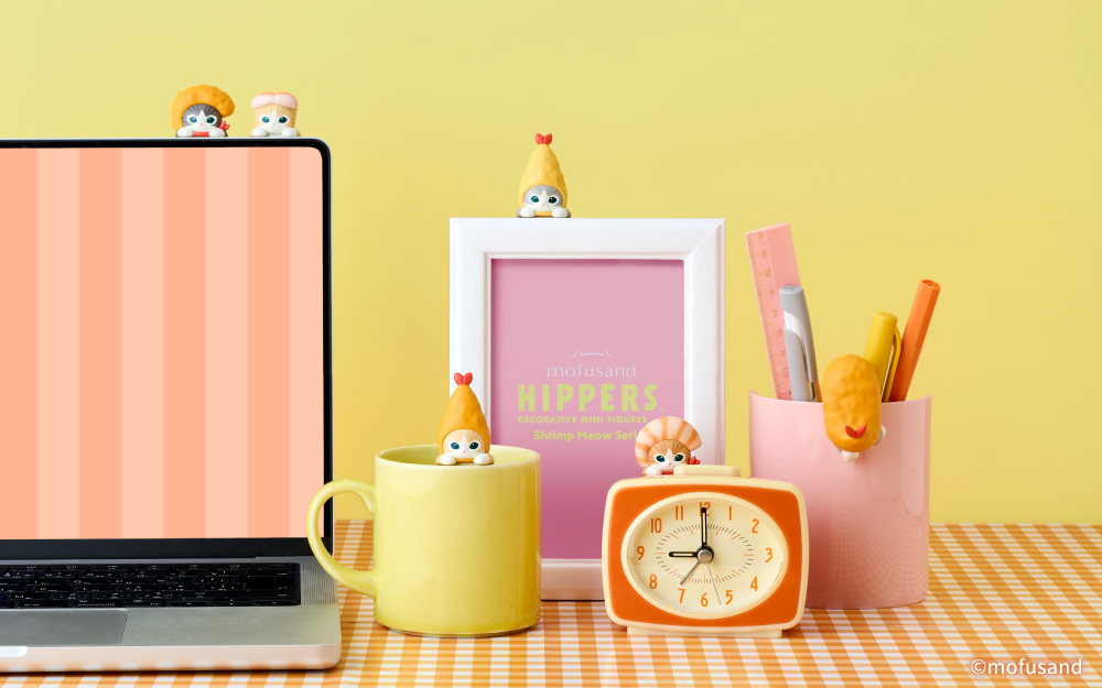 Brightly themed promotional image for mofusand HIPPERS- Shrimp Meow Series. On the left side of the image, set against a bright yellow background atop an orange checked table cloth set a laptop computer, yellow mug, white frame, orange analog clock and pink writing utensil cup. Mofusand HIPPERS Shrimp Meow figures from left to right atop the various items include: Popcorn Shrimp Meow, Shrimp Sushi Meow, Fried Shrimp Meow, Shrimp Tempura Meow, Prawn Meow, and Panko Shrimp Meow