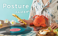 Image shows the upper body of a person in a floral button down shirt sitting with the red/orange Lobster Posture Pal. On the wooden table in the image, white and yellow flowers are beside a music record, and a bowl of food, the person s seen on a yellow cell phone. Text says "Posture Pal" in english, as well as the product name in Japanese. The image is set on a light blue background.
