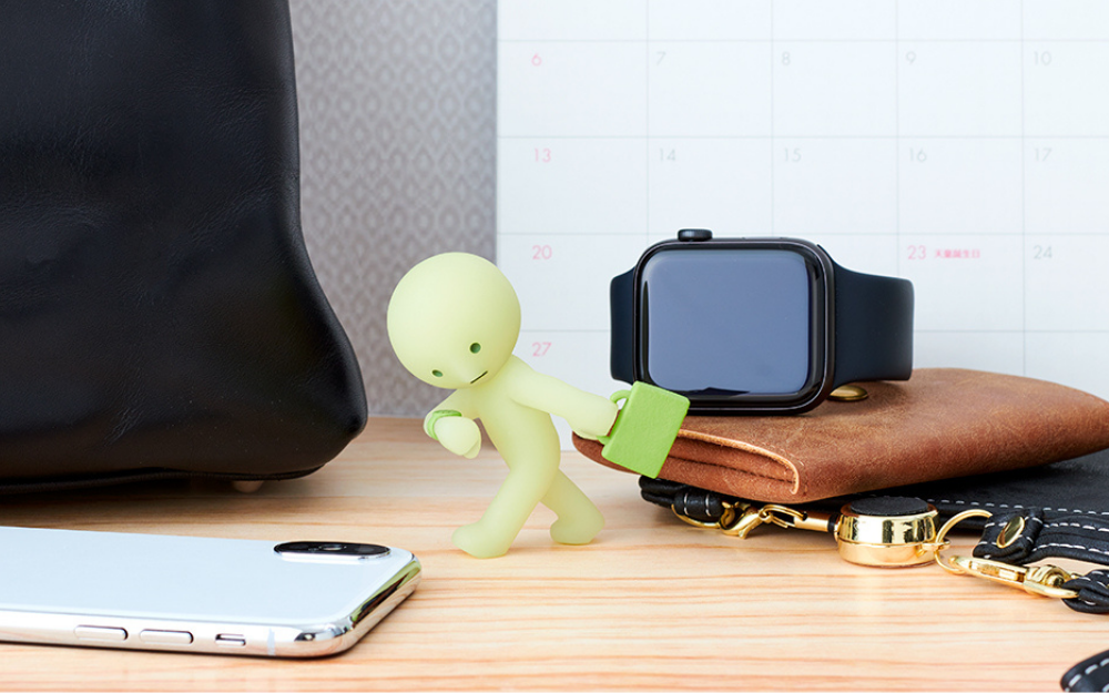 closeup of smiski briefcase on a desk setup with smart watch and phone props